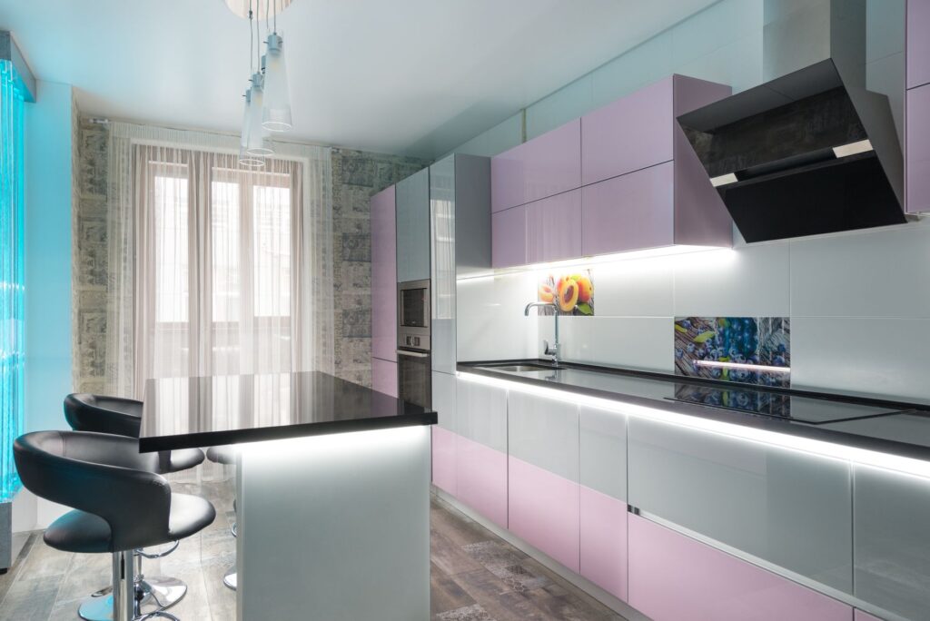 Black counter with chairs placed in modern kitchen with colorful cupboards near extractor fan and kitchenware against wind…