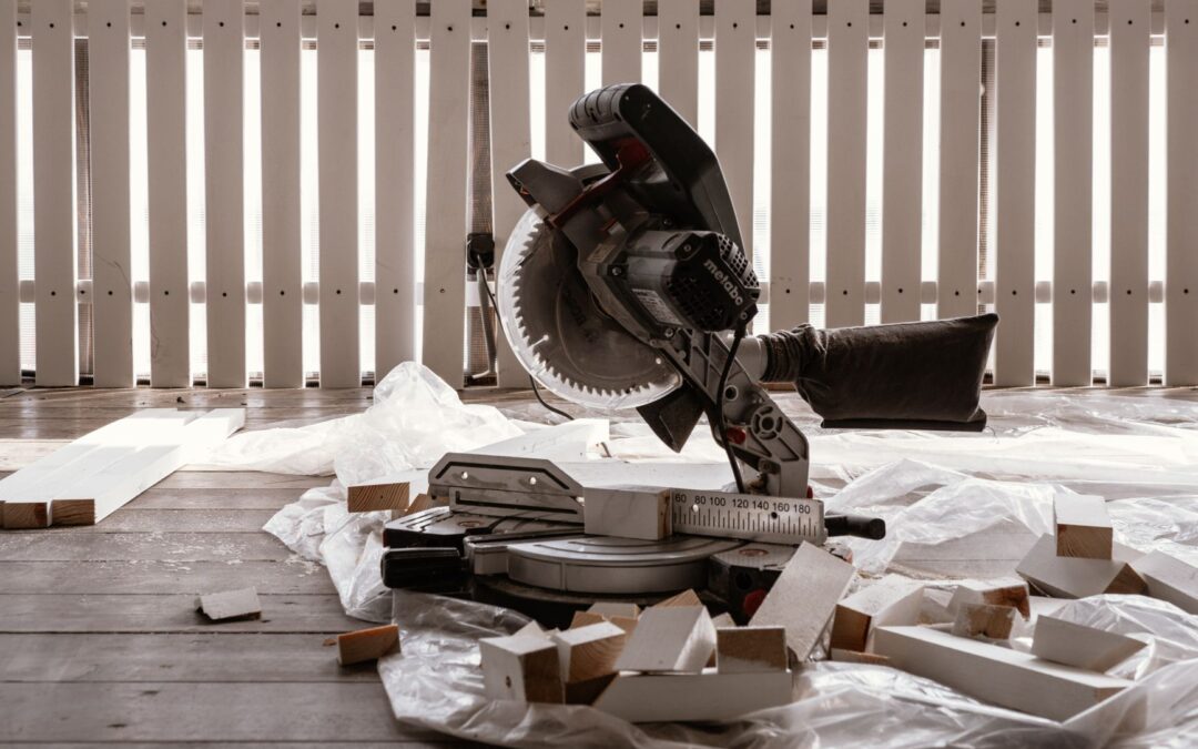 A circular saw on a wooden terrace with cut wood pieces and a white fence.