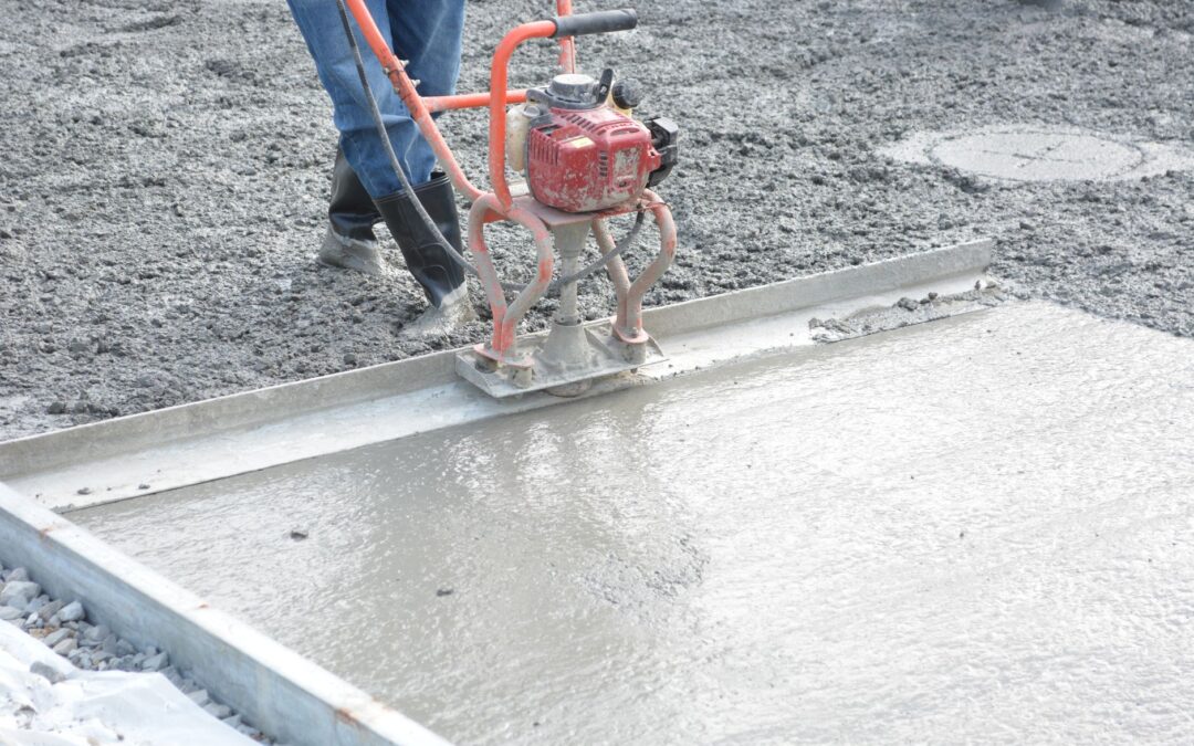 A construction worker operates a power trowel to smooth freshly poured concrete on a construction site.