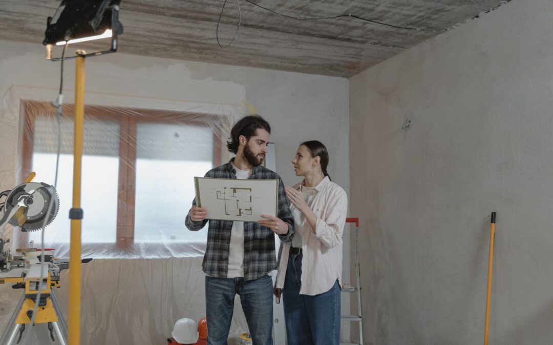 A couple reviews a blueprint in a partially renovated room, planning home improvements.
