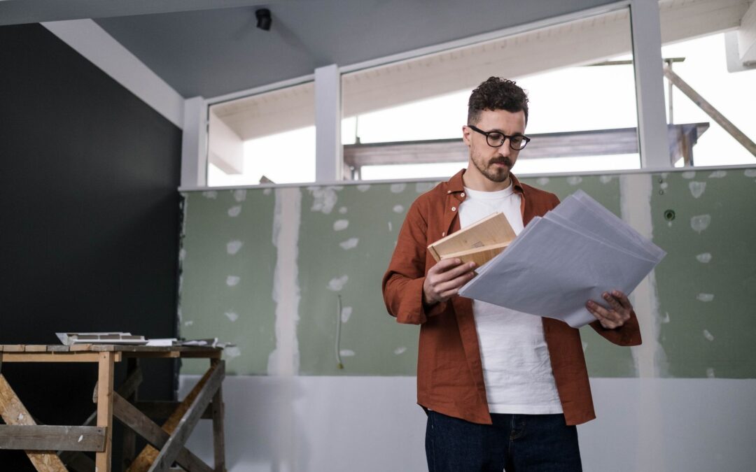 A focused adult male architect examines construction plans indoors, showcasing project management.