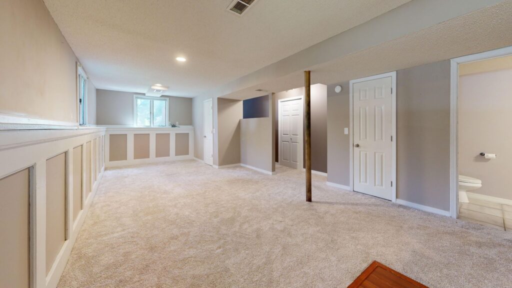 Bright and clean modern basement with carpet flooring and recessed lighting.
