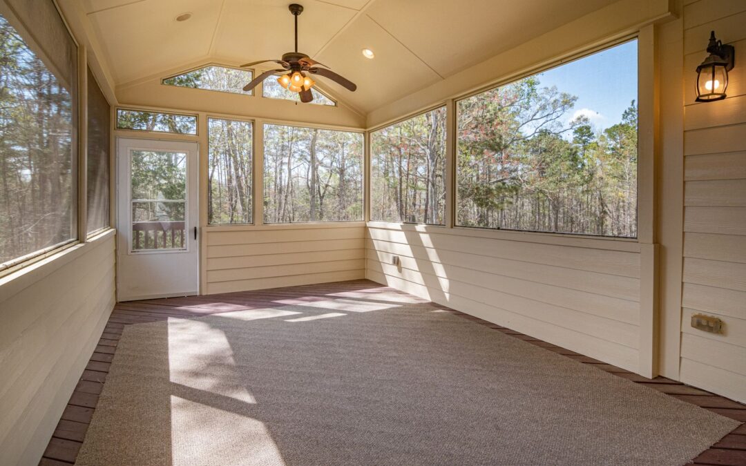 Bright empty porch with ceiling fan and large glass windows revealing a forest view.