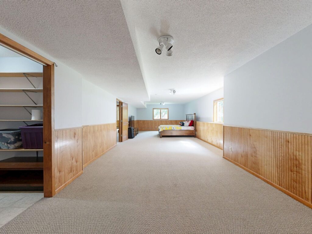Empty basement room with wooden paneling and carpet, offering ample space for various uses.