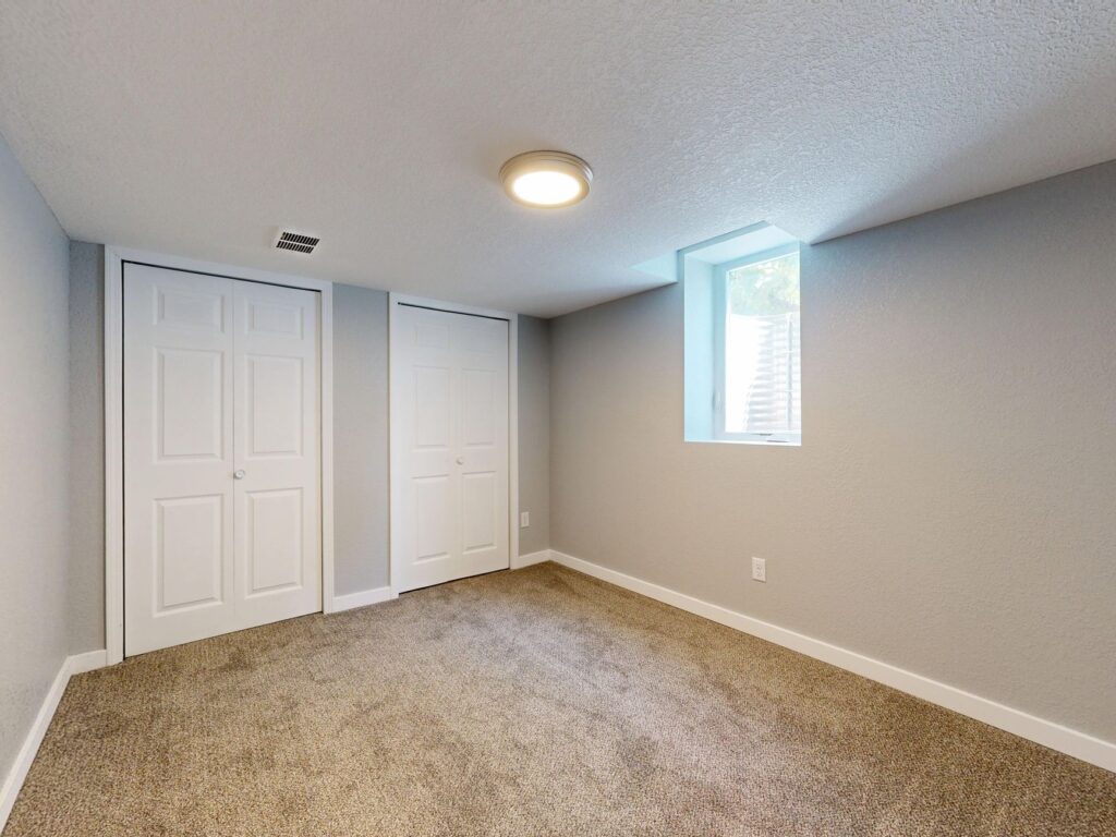Minimalistic empty room with carpet, two white doors, and natural light from a window.