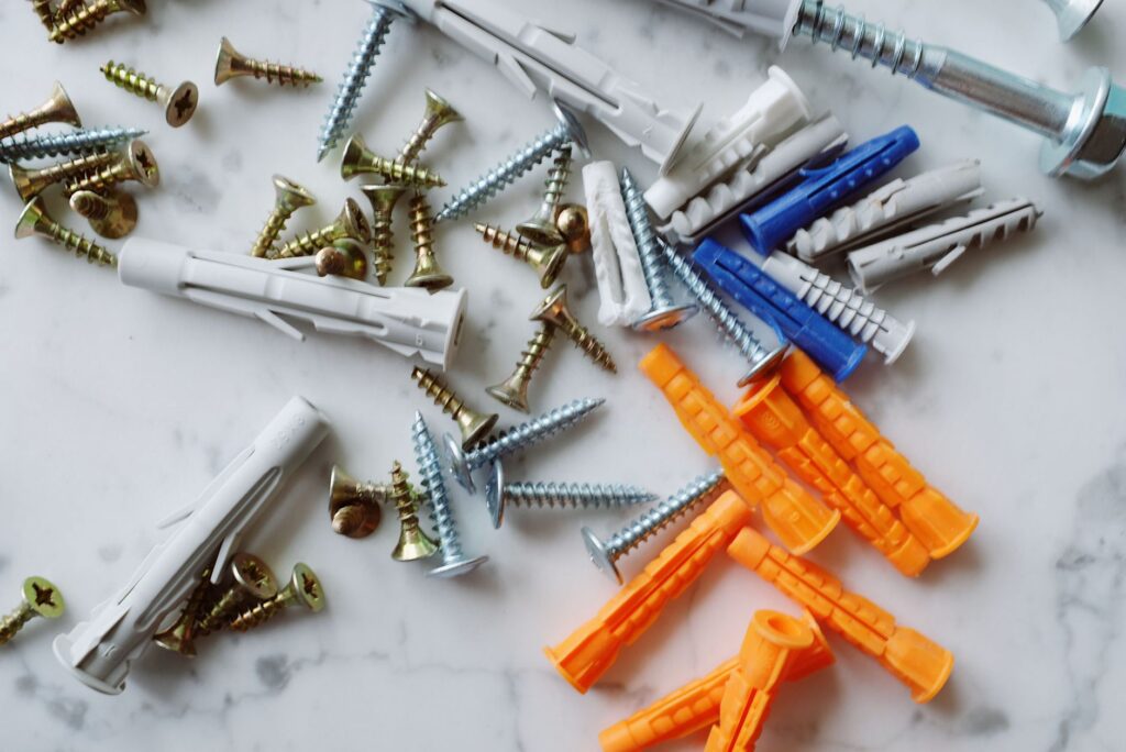 Set of various multicolored plastic dowels with assorted metal screws of different sizes placed on white marble table in m…