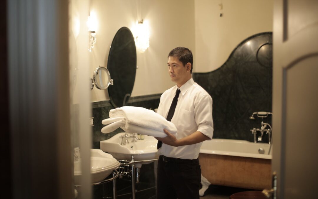 Side view of young male employee holding stack of white towels while standing in bathroom of luxury hotel