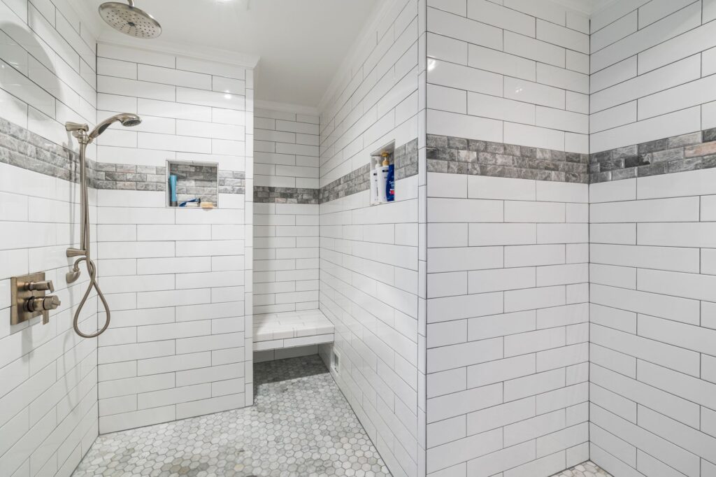 Sleek and minimalistic white tiled walk-in shower with modern fixtures and mosaic floor.