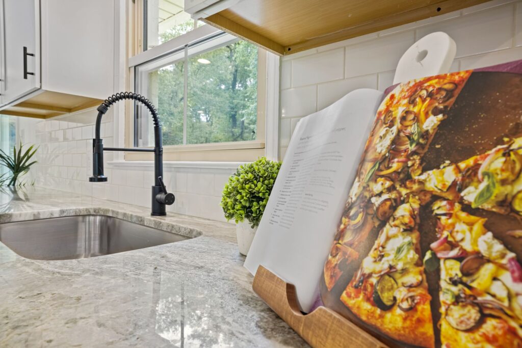 Stylish kitchen featuring a marble countertop, modern sink, and an open cookbook with a pizza recipe.
