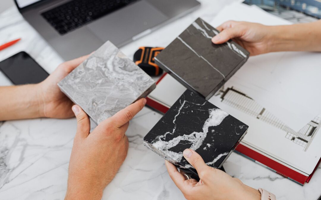 Two architects selecting marble tile samples on a desk in an office setting.