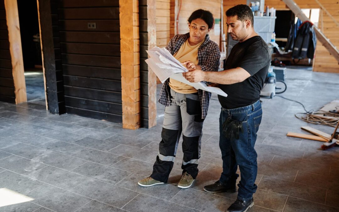 Two workers examining blueprints inside a building under construction, showcasing teamwork.