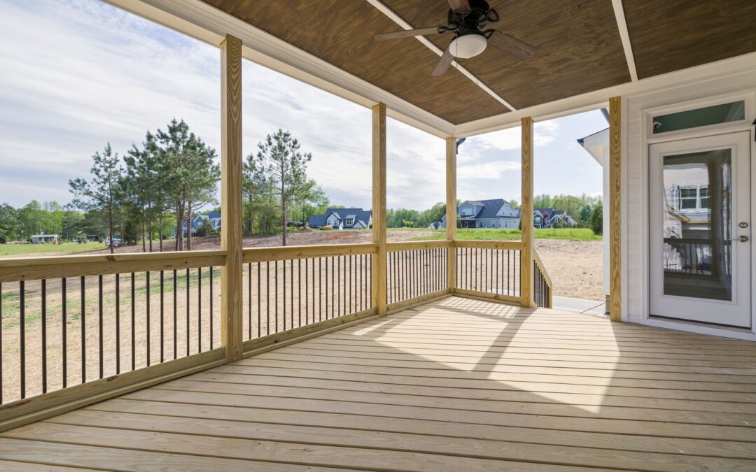 A bright wooden porch with ceiling fan and glass door, overlooking a grassy area.