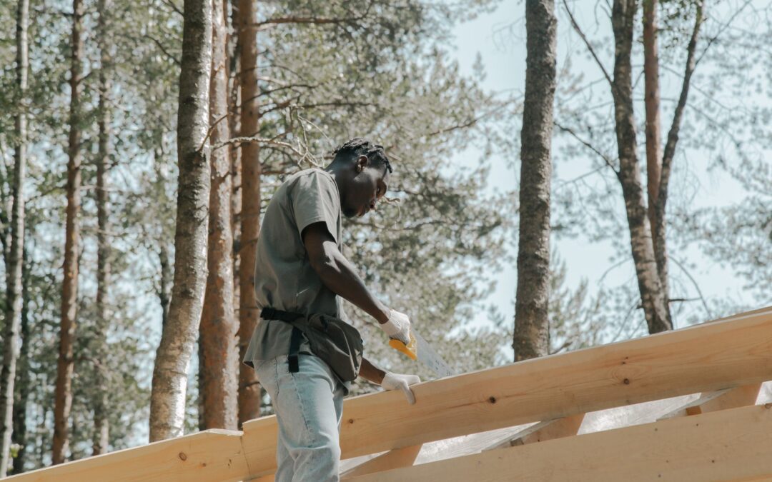 A construction worker sawing wood on a building project outdoors in a forest setting.