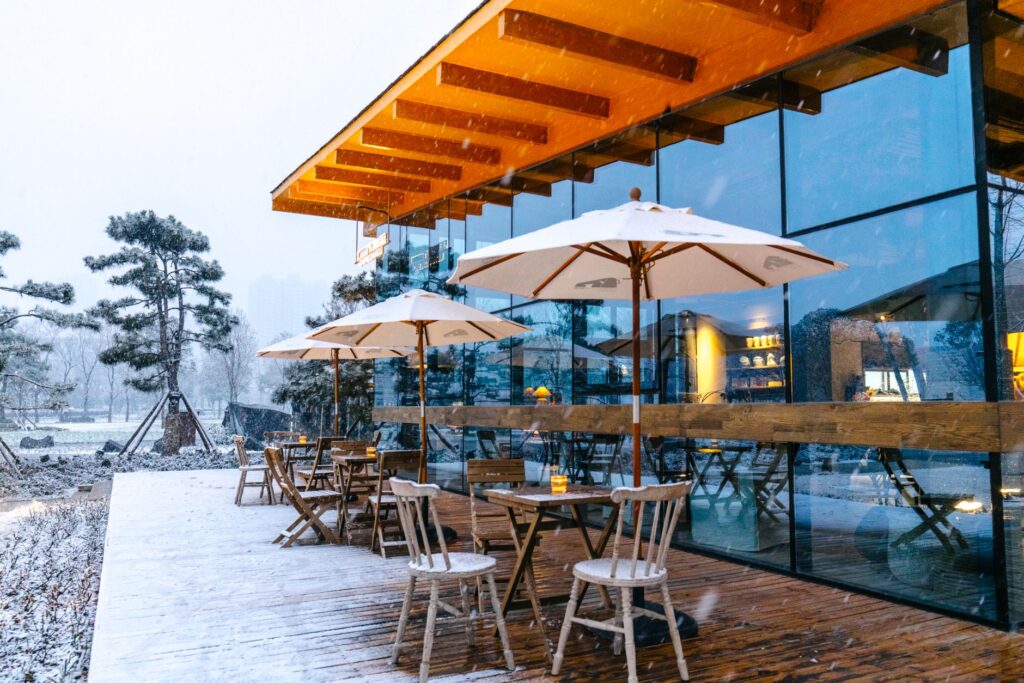 A cozy outdoor cafe with beach umbrellas surrounded by snow in a wintery setting.
