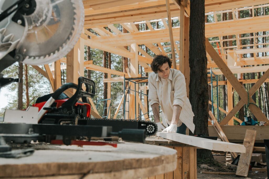 A focused carpenter working with tools at a wooden construction site outdoors.
