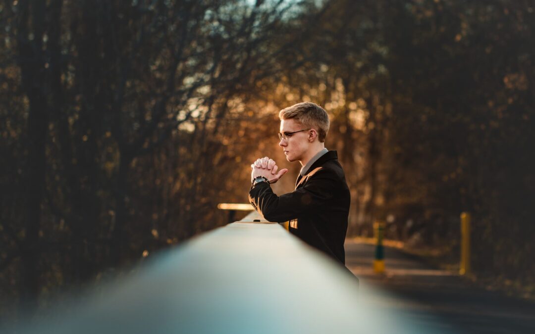 A man in a suit gazes thoughtfully from a bridge during a golden sunset in a park.