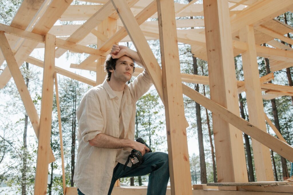 A man in casual attire ponders amidst a wooden structure at a construction site.