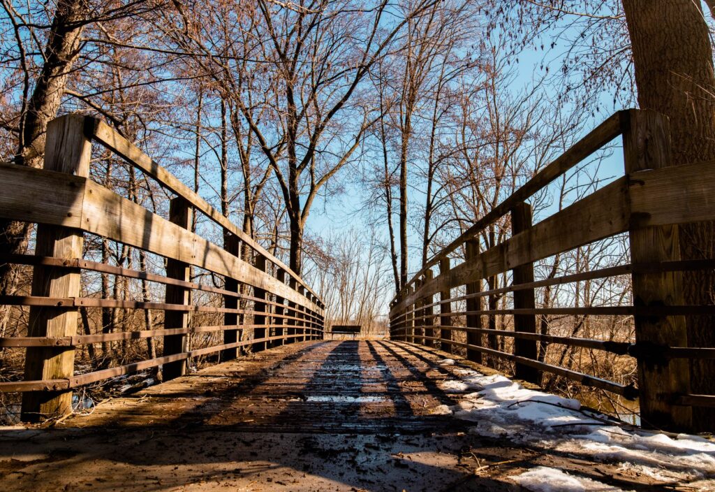 A picturesque wooden bridge in a snowy winter setting, surrounded by bare trees in Ann Arbor, Michigan.