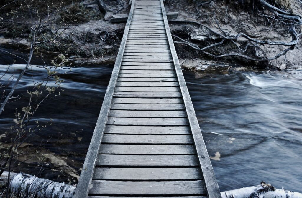 A tranquil wooden footbridge over a flowing river in Michigan wilderness.