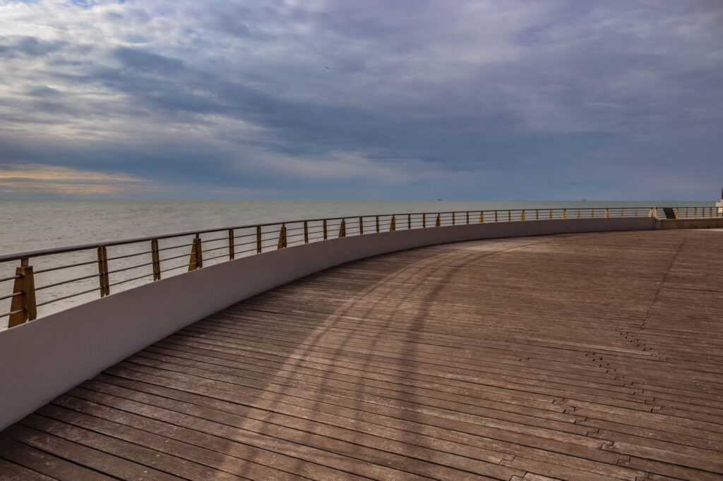 Beautiful outdoor scene of an ocean view with an expansive wooden deck and railings at sunset.