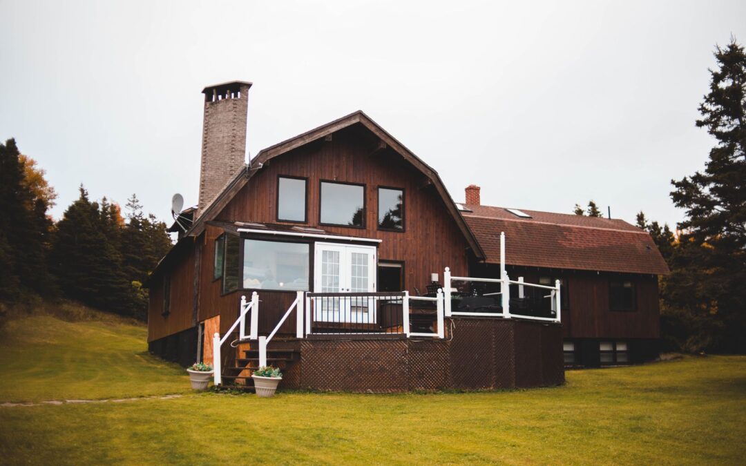 Beautiful wooden house with a chimney surrounded by lush forest and green grass, offering tranquility.
