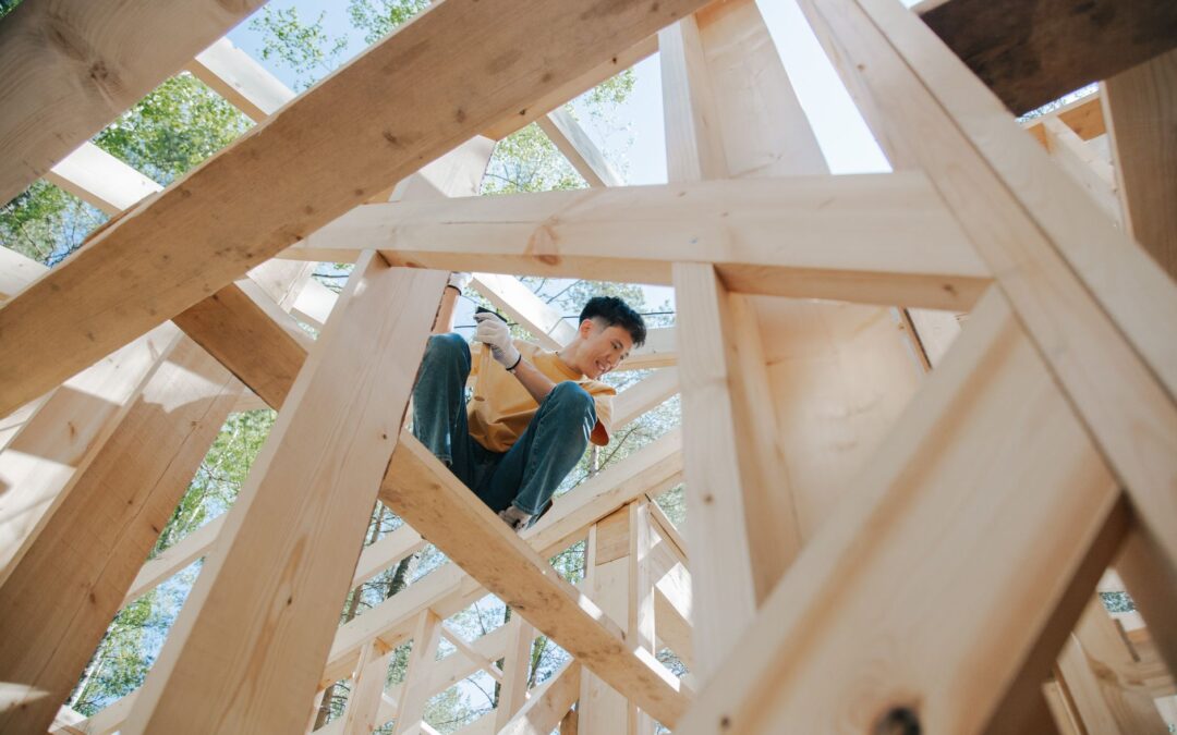 Carpenter working on the wooden structure of a house at a construction site under the sun.