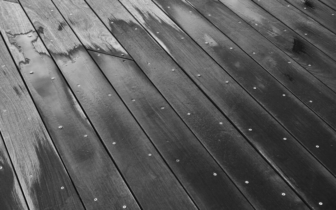 Close-up of a wet wooden floor with visible grain and screws in black and white.