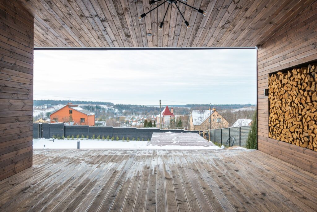 Cozy wooden deck with stacked firewood and scenic snowy village view in winter.