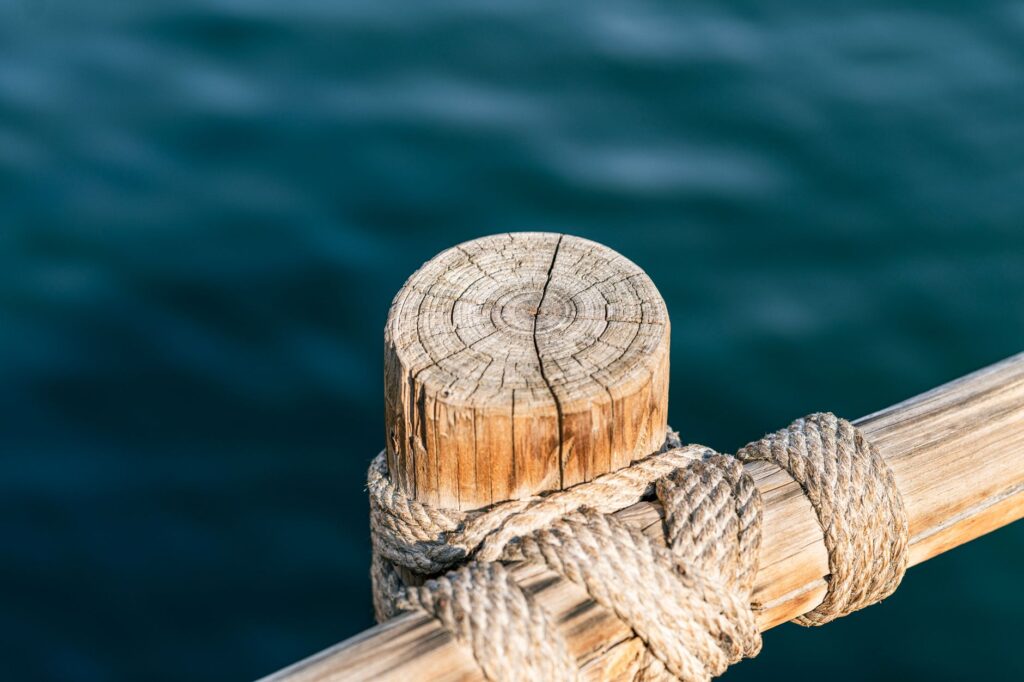 Detailed close-up of a dock's wooden post wrapped with rope against the sea in Dubai Marina.
