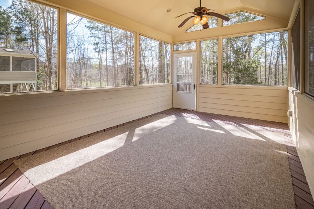 Spacious sunroom featuring glass panels and a ceiling fan, offering scenic woodland views.