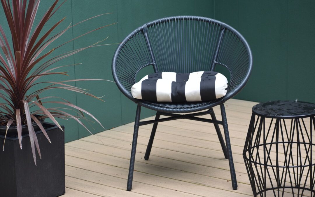 Stylish outdoor patio scene featuring a modern black chair with a striped cushion, a potted plant, and a wire stool.