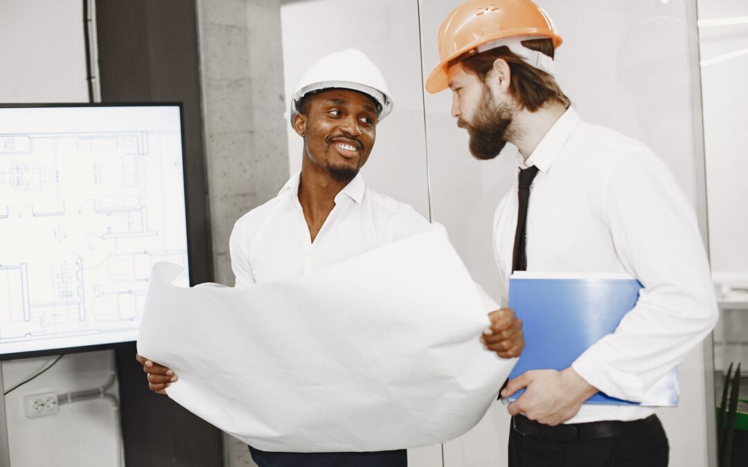 Two architects in hard hats discuss blueprints in a modern office setting, highlighting teamwork and planning.