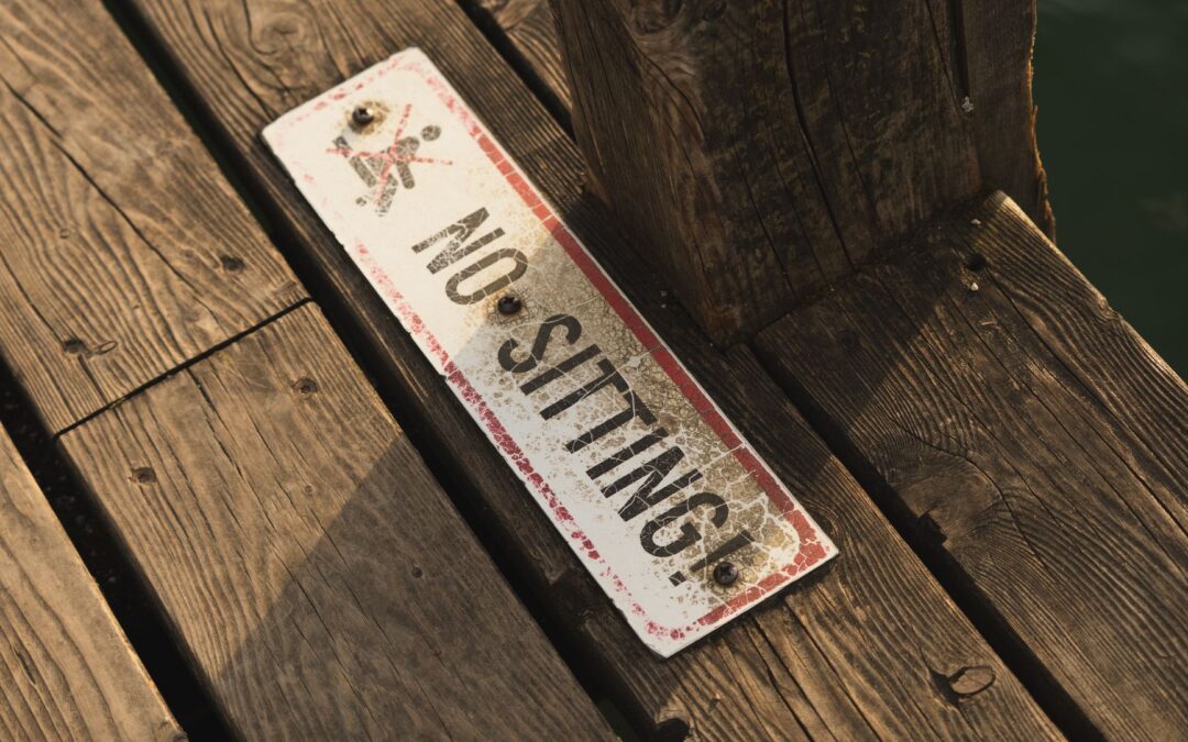 Weathered wooden deck with a distressed 'No Sitting' sign, highlighted by natural light, creating an earthy feel.