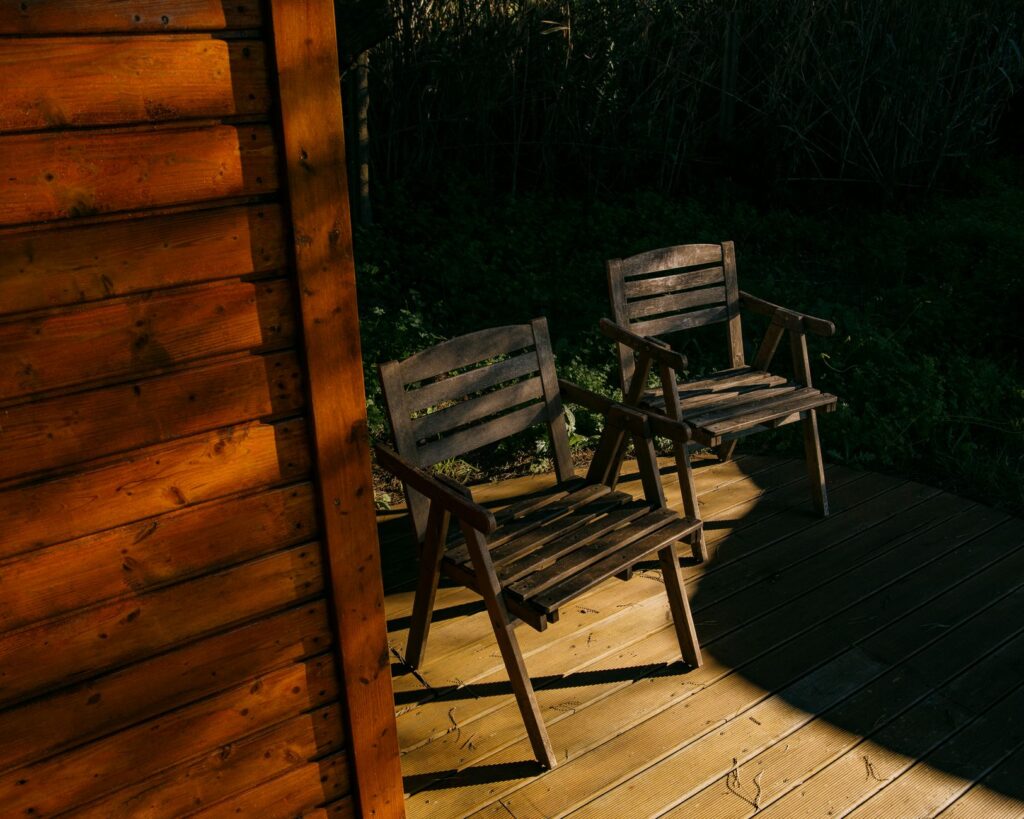 Wooden chairs on a sunlit deck next to a wooden cabin, creating a serene outdoor setting.