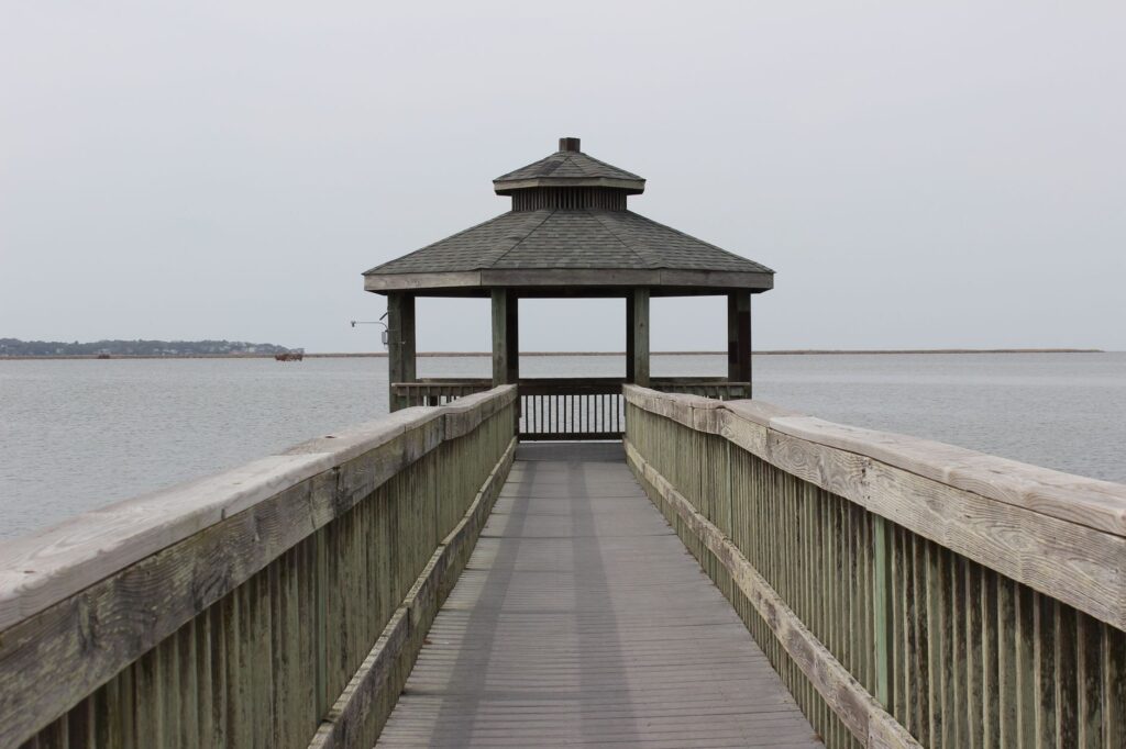 Wooden gazebo on a pier extending into a calm lake, perfect for relaxation and nature views.